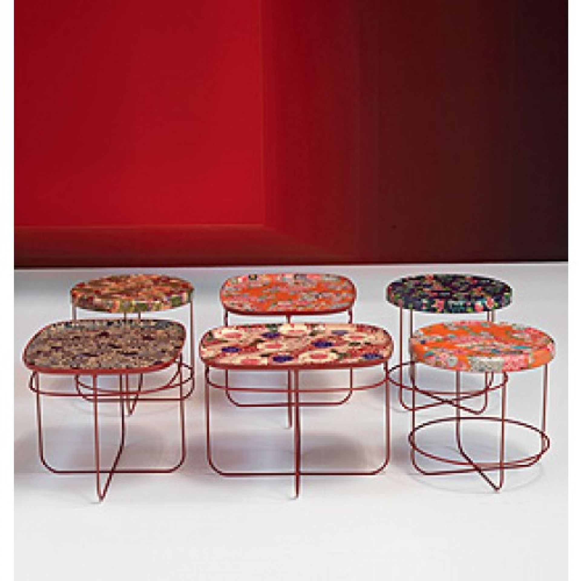 Sechs farbenfrohe Ukiyo Tische von Moroso mit floralen Mustern und roten Metallgestellen vor rotem Hintergrund.